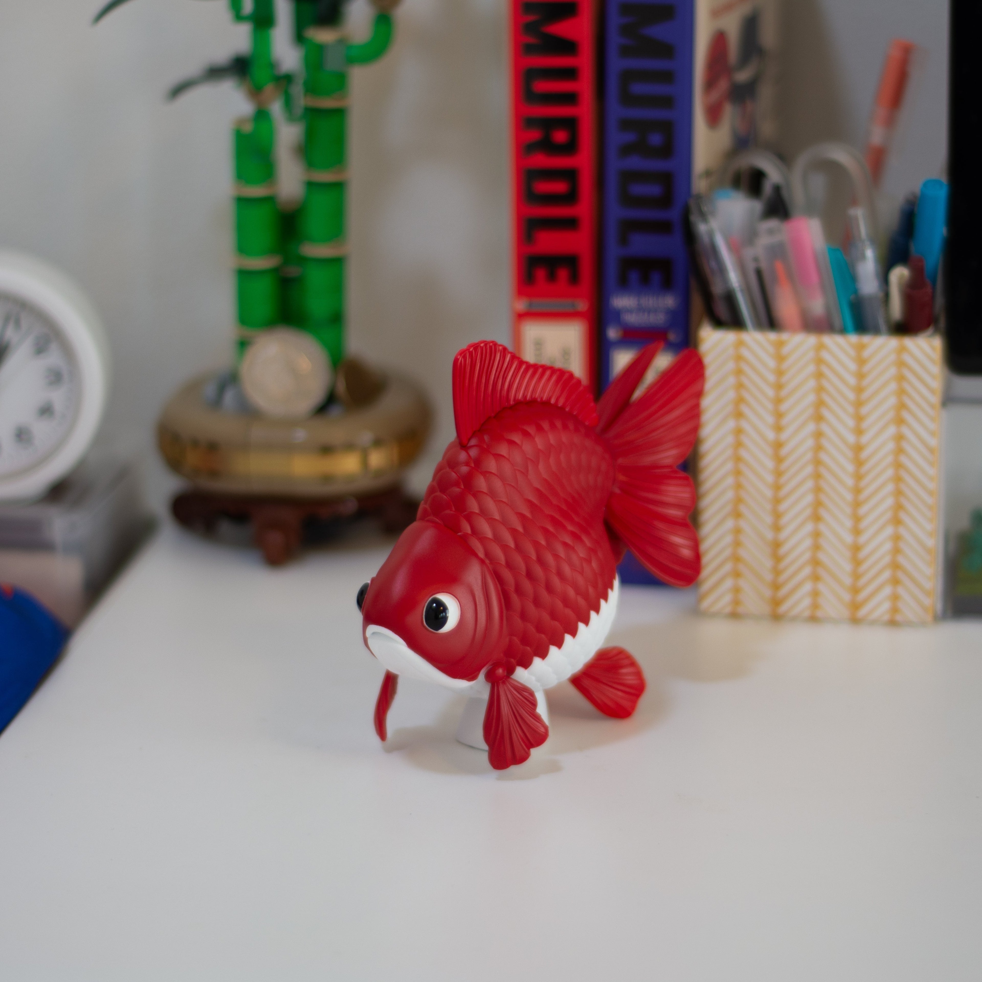 Red and white fish figurine on a desk with various items in the background
